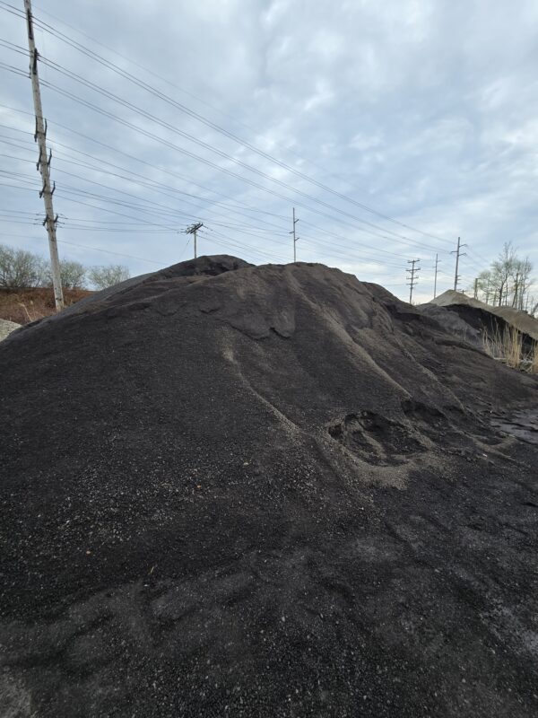 Large mound of black coal piled outdoors with power poles and lines in the background on a cloudy day.